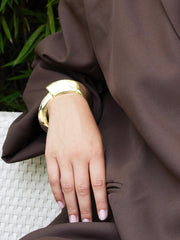 Goudkleurig plat organisch scharnierarmband van Ellen Beekmans met een glad, modern design en natuurlijke vormen.